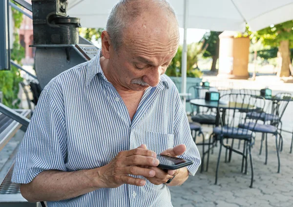 一位老人在咖啡店等早上的咖啡时拿着一部手机 — 图库照片