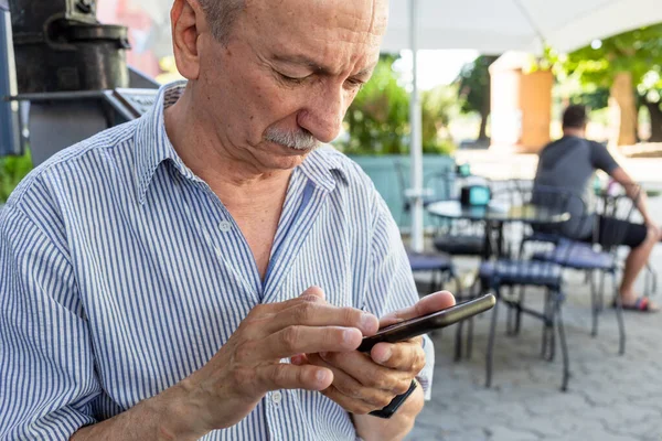 一位老人在咖啡店等早上的咖啡时拿着一部手机 — 图库照片
