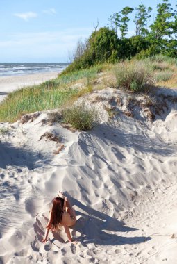 Güneşli bir yaz gününde beyaz kum tepeleri arasında poz veren tamamen çıplak genç bir kadın.