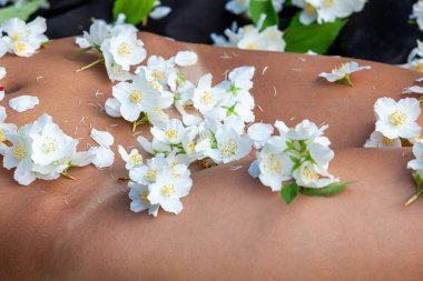 Güzellik, şehvet ve çıplaklık konsepti. Genç ve çıplak bir kadının romantik görüntüsü çimenlerde yatar ve yasemin çiçekleriyle süslenir..