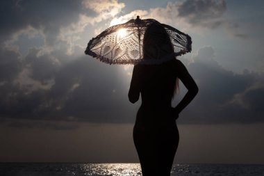 Deniz kenarında tamamen çıplak bir kadın beyaz dantelli güneş şemsiyeli deniz melteminin tadını çıkarıyor.