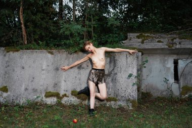 Genç bir kadın ormanda beton levhaların arasında kırmızı bir elmayla üstsüz poz veriyor..