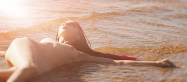 Kırmızılı, çırılçıplak genç bir kadın deniz kenarında doğanın tadını çıkarıyor.