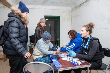 CHASIV YAR, DONETSK REG, UKRAINE - Mar. 09, 2024: Gönüllü görevden bir kadın doktor Frida Ukrayna, tıbbi yardım isteyen hastaların kan basıncını ölçüyor