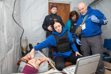 SIVERSK, DONETSK REG, UKRAINE - Mar. 10, 2024: Frida Ukrayna Gönüllü Görevi 'nden bir kadın ultrason doktoru yerel bir kadına ultrason taraması yaparken görüldü..