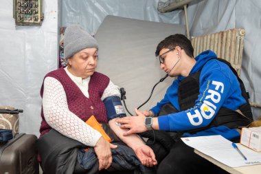 SIVERSK, DONETSK REG, UKRAINE - Mar. 10, 2024: Frida Ukrayna Gönüllü Görevi 'nden bir doktor yerel bir kadının kan basıncını ölçerken görüldü.