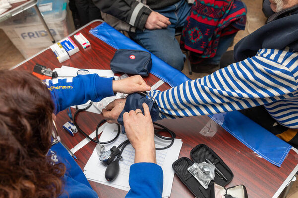 CHASIV YAR, DONETSK REG., UKRAINE - Mar. 09, 2024: A woman doctor from the volunteer mission Frida Ukraine is measuring the blood pressure of patients seeking medical assistance