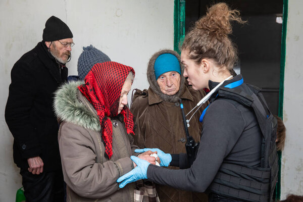 CHASIV YAR, DONETSK REG., UKRAINE - Mar. 09, 2024: A young woman doctor from the volunteer mission Frida Ukraine is giving medical advice to elderly women seeking help.