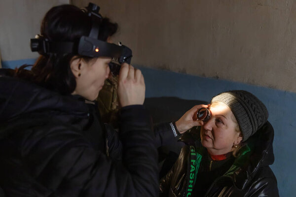 SIVERSK, DONETSK REG., UKRAINE - Mar. 10, 2024: A woman ophthalmologist from the volunteer mission Frida Ukraine is examining the vision of an elderly woman in  underground shelter