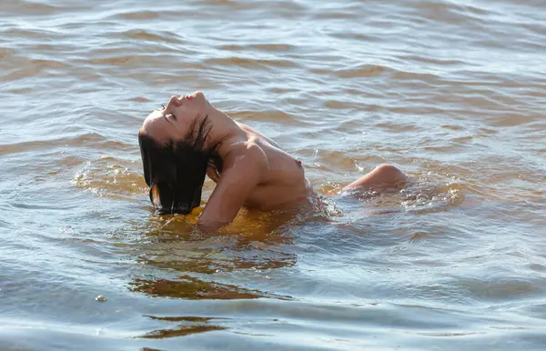 Deniz kenarında çıplak poz veren güzel bir kadın denizin ve doğanın tadını çıkarıyor. Sağlıklı ve mutlu bir yaşam tarzı. Gençlik ve çıplaklık kavramı