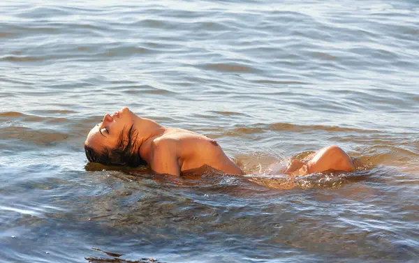 Deniz kenarında çıplak poz veren güzel bir kadın denizin ve doğanın tadını çıkarıyor. Sağlıklı ve mutlu bir yaşam tarzı. Gençlik ve çıplaklık kavramı