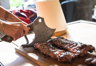 IV, UKRAINE - Mayıs. 18, 2024: Bir garson, popüler bir lokantada pirzola ile ızgara domuz pirzolası doğruyor, bir bardak bira ve bir şişe yakınlardaki masada oturuyor ve kırsal bir yemek atmosferi yaratıyor.