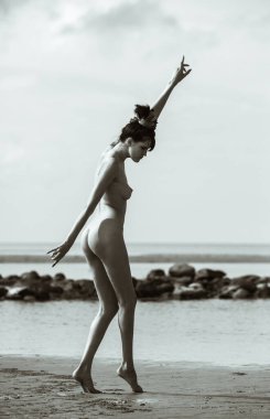 Deniz kenarında çıplak poz veren genç, güzel ve duygusal bir kadın. Güzellik, yaşam tarzı ve çıplaklık kavramı.
