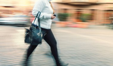 Sokakta yürüyen bir kadın cep telefonuyla konuşuyor. Şehir hayatı bulanık bir hareketle. 