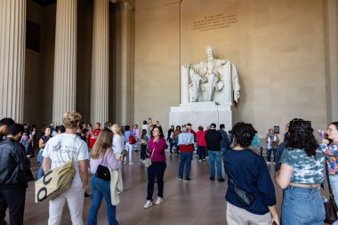 Washington DC, ABD - 10 Ekim 2022: Abraham Lincoln 'ün devasa mermer heykelinin arka planında bir grup turist, yüksek kolonlarla çevrili büyük bir salonda oturuyorlar..