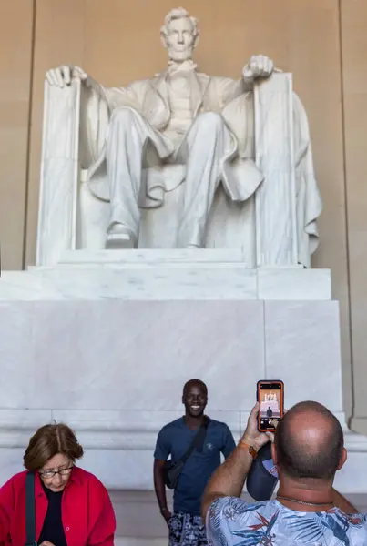 stock image Washington DC, USA - Oct. 10, 2022: Tourists take photos in front of a colossal marble statue of Abraham Lincoln seated in a grand hall surrounded by towering columns.