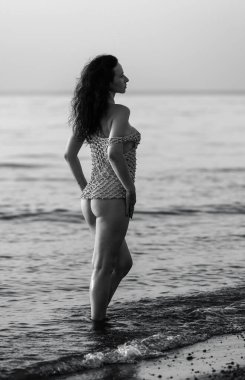 Genç ve güzel bir kadın sahilde yarı çıplak poz veriyor sığ suda duruyor.