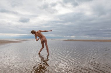 Denizin sığ sularında çıplak poz veren genç ve güzel bir bayan dansçı. Güzellik, zarafet, yaşam tarzı ve çıplaklık kavramı.