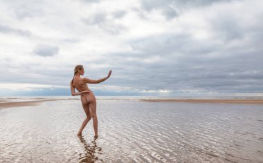Denizin sığ sularında çıplak poz veren genç ve güzel bir bayan dansçı. Güzellik, zarafet, yaşam tarzı ve çıplaklık kavramı.