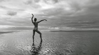 Denizin sığ sularında çıplak poz veren genç ve güzel bir bayan dansçı. Güzellik, zarafet, yaşam tarzı ve çıplaklık kavramı.