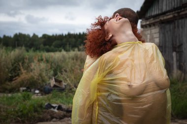 İnsanlar arasındaki sevgi ve bağ. Çıplak bir adam ve kadın, sırtları birbirine dönük, kırsalda plastiğe sarılmış bir şekilde duruyorlar.