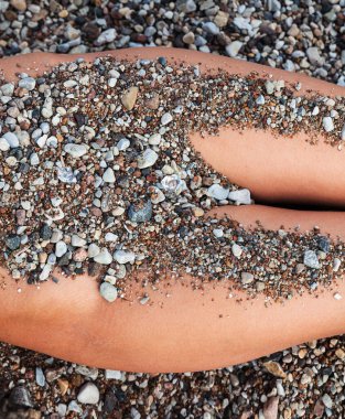 Bir kadın doğal bir ortamda yan yatar, çıplak bedeni küçük taşlar ve çakıl taşlarıyla kısmen kamufle olur. Organik renkler çevreyle uyumlu bir karışım oluşturuyor..