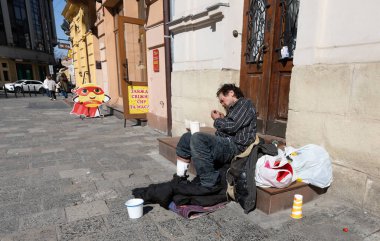 Lviv, Ukrayna - Mar. 22, 2025: Lviv 'in canlı sokaklarında, evsiz bir adam merdivenlerde dinleniyor, eşyalarıyla çevrili, dayanıklılığını somutlaştıran ve kentsel hayatın katı gerçekleriyle..