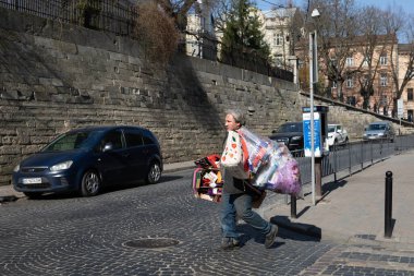 Lviv, Ukrayna - Mar. 22, 2025: Bir şahıs, çöp torbaları taşıyarak topluma katkıda bulunurken renkli malları dengeleyerek kaldırım taşlarından caddelerde geziniyor..
