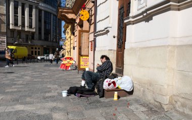 Lviv, Ukrayna - Mar. 22, 2025: Evsiz bir adam, Lviv 'deki bir binaya karşı dinleniyor, etrafı eşyalarıyla çevrili, canlı bir şehirde zorluklarla karşılaşanların gücünü yakalıyor..