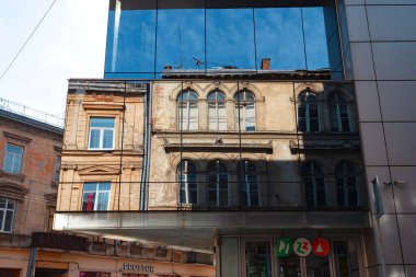 Lviv, Ukrayna - Mar. 22, 2025: Gündüz vakti modern cam mimari Lviv 'deki tarihi binaların karmaşık detaylarını güzel bir şekilde yansıtıyor, çarpıcı bir yan yana dizilme yaratıyor..