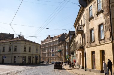 Lviv, Ukrayna - Mar. 22, 2025: Lviv 'deki kaldırım taşlı sokaklar, yerliler yürürken güneşin altında parlıyor. Tarihsel yapılar, şehirlerin zengin mimari mirasını gözler önüne sererek dimdik ayakta duruyorlar..