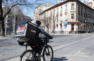 Lviv, Ukrayna - Mar. 22, 2025: Bir bisikletçi, güneşli bir günde, hareketli şehir manzarasında gezinirken, Ukrayna 'nın canlı caddelerinde yiyecek dağıtır..