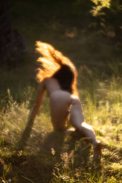 Soft focus blurred image of a young nude woman in sun light on the forest background. Image in a soft romantic and vintage style