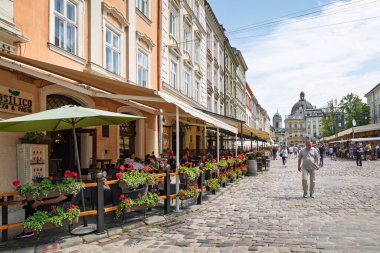 LVIV, UKRAINE - Haziran. 20, 2021: İnsanlar renkli kafeler ve çiçek vitrinleriyle dolu kaldırım taşlı caddelerde yürüyor. Tarihi mimari şehir merkezinde büyüleyici bir atmosfer yaratıyor..