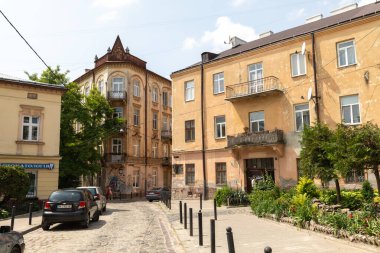 LVIV, UKRAINE - Haziran. 20, 2021: Eşsiz tarihi mimari eski kasabadaki kaldırım taşlı caddeleri çiziyor. Ağaçlar ve bitkiler bu canlı bölgenin güzelliğini arttırır, keşifleri teşvik eder..