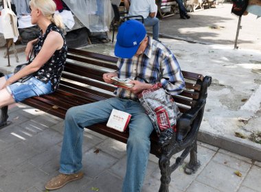 LVIV, UKRAINE - Haziran. 20, 2021: Bir kartpostal koleksiyoncusu, işlek şehir bit pazarındaki ahşap bir bankta bulduğu son bulguları inceliyor. Yakınlarda, sıcak havanın tadını çıkaran başka bir müşteri daha var..