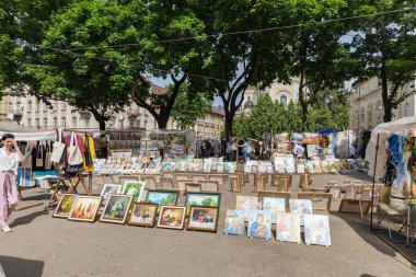 LVIV, UKRAINE - Haziran. 20, 2021: Sanat severler yerel el işleri, resimler ve el yapımı mallarla dolu canlı bir bit pazarını keşfediyorlar. Piyasa ziyaretçilerle ve parlak ağaçların altında renkli gösterilerle dolu..