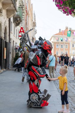 LVIV, UKRAINE - Haziran. 20, 2021: Vatandaşlar ve turistler, robot kostümlü bir sokak sanatçısıyla etkileşime geçerek tarihi sokaklarda dolaşıyorlar. Atmosfer canlı ve canlı..