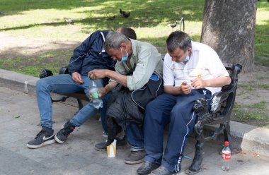 LVIV, UKRAINE - Haziran. 20, 2021: Şehir merkezindeki bir bankta oturan üç adam, otururken yalnızlık anlarını paylaşıyorlar. İnsanlar geçerken, mallarıyla meşgul gibi görünüyorlar..