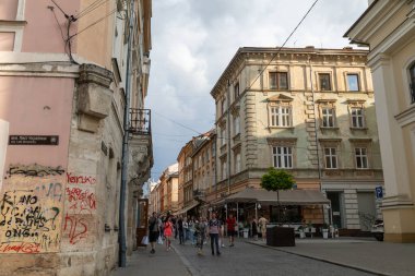 LVIV, UKRAINE - Haziran. 20, 2021: İnsanlar eşsiz binalarla çevrili kaldırımlı caddelerde yürüyor. Tarihsel mimari ve modern yaşamın karışımı Lviv 'de canlı bir şehir atmosferi yaratır..