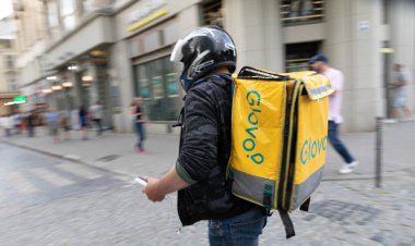 LVIV, UKRAINE - Haziran. 20, 2021: Siyah ceketli ve miğferli bir teslimatçı kalabalık caddede elinde bir telefonla dolaşırken, elinde sarı bir yemek paketi, canlı şehir yaşamını gözler önüne seriyor..