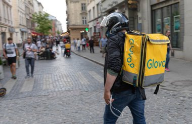 LVIV, UKRAINE - Haziran. 20, 2021: kask takan bir kurye teslimat çantasıyla kalabalık caddelerde yürüyor. İnsanlar şehrin canlı atmosferinin tadını çıkararak geziyorlar..