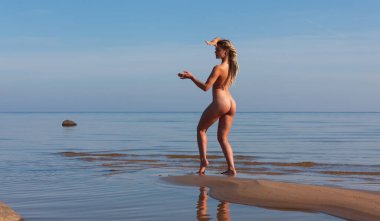 Genç bir kadın bir yaz öğleden sonra sahilde çıplak poz veriyor.