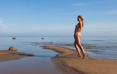 Rasta saçlı genç bir kadın güneşli bir günde sahilde çıplak poz verir. Güzellik, gençlik ve çıplaklık kavramı.