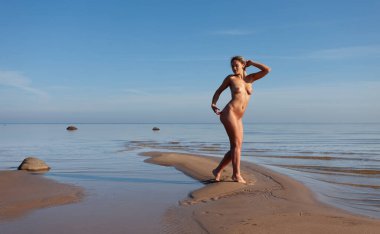 Rasta saçlı genç bir kadın güneşli bir günde sahilde çıplak poz verir. Güzellik, gençlik ve çıplaklık kavramı.