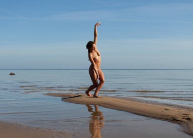 Rasta saçlı genç bir kadın güneşli bir günde sahilde çıplak poz verir. Güzellik, gençlik ve çıplaklık kavramı.