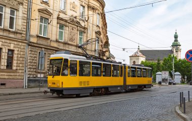 Lviv, Ukrayna - Haziran. 2025: Sarı bir tramvay tarihi şehir merkezinde bir kaldırım taşı caddesinde ilerliyor..