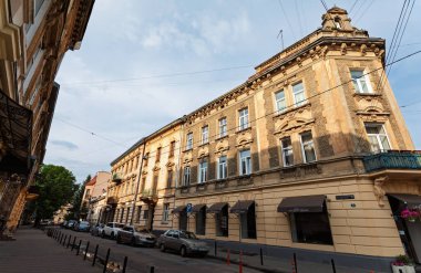 Lviv, Ukrayna - Haziran. 2001, 2025: Tarihi Lviv şehrinde eski binalar ve park edilmiş arabaların yer aldığı güneşli bir sokak manzarası.