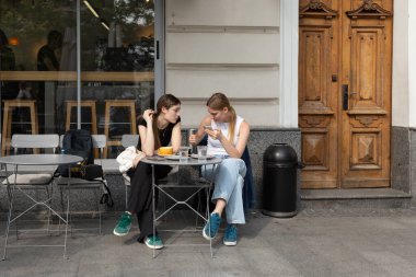 Lviv, Ukrayna - Haziran. 01, 2025: İki genç kadın açık bir kafe masasında oturuyor, biri telefona bakıyor..