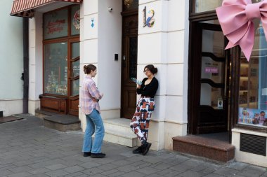Lviv, Ukrayna - Haziran. 01, 2025: Güneşli bir günde iki genç kadın bir mağaza girişinin yanında durmuş, bir binanın önünde sohbet ediyorlar..
